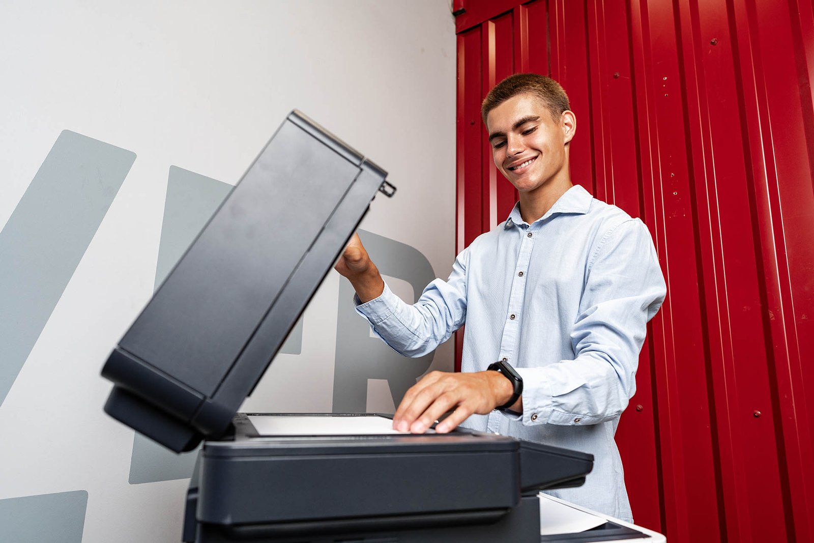 Positive young man using printer in the modern office